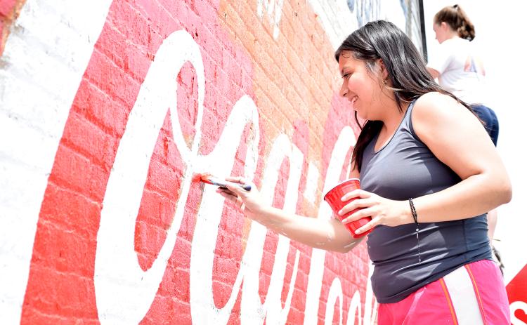 Alondra Arevalo carefully paints over the red around the white letters on the mural on West Main Street. (Photo by Sinclair)
